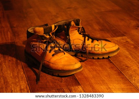 A warm picture of a pair of worn out, rusty brown winter boots on a parquet floor. 