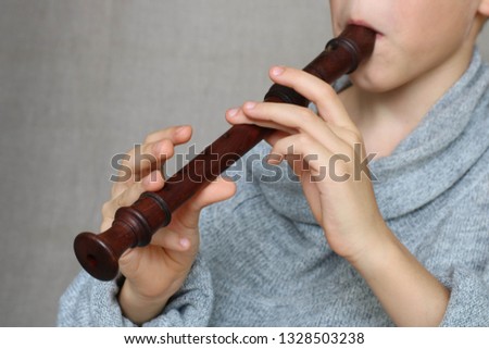 the child's hands play the dark brown wooden flute on a grey background