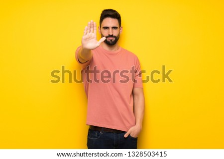 Handsome man over yellow wall making stop gesture denying a situation that thinks wrong