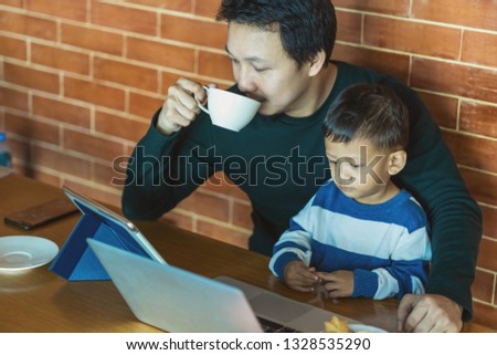 Asian single dad with son are looking the cartoon via technology laptop and drinking coffee with work when living in loft house for Self learning or home school,Family and single father concept