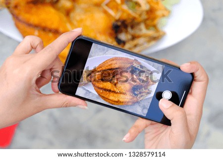 Women use smartphones to record images of food Fried fish are placed on the table in the kitchen.