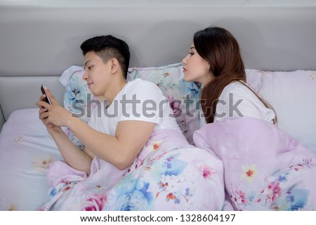 Picture of young woman snooping phone of her husband while lying on the bed