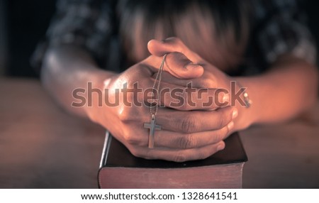 Young male praying on bible with cross in hands. christian concept.