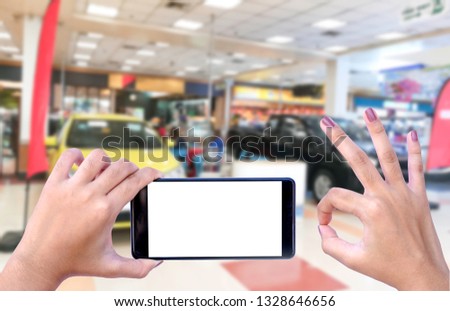 Mockup hands (in" ok" sign) holding and showing mobile smart phone with empty white screen on car showroom blurred background. Funding approved, loan approval for buy new car  concept. Clipping path .