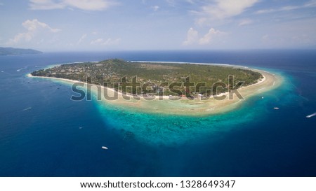 Gili island from the top with a drone point of view. In the picture we can see the coral and some boats in the blue ocean