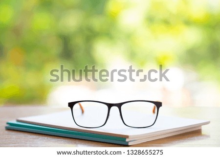 Black eyeglasses with three white notebook on wooden table, Bokeh garden background, Close up & Macro shot, Selective focus, Stationery concept