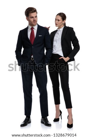 couple in business suits looking serious with hands on pockets and shoulder on white background