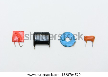 Four different type and color capacitors. Ceramic, film and metal type capacitors. Square tiny red, black rectangular, blue round, orange film capacitor.   On white background
