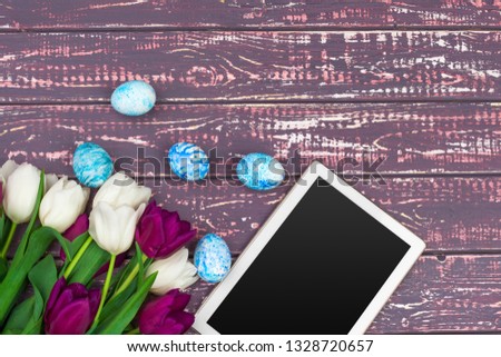 tablet screen for message and colorful tulips and easter eggs on wooden background