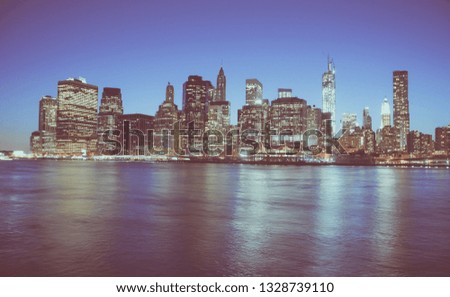 Iconic view of world famous New York Financial District and the Lower Manhattan at night viewed from the Brooklyn Bridge Park. Low contrast color image.