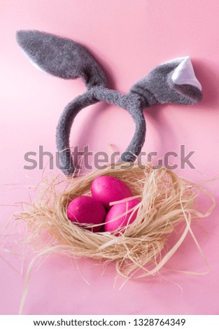 3 Easter eggs in the nest, rabbit ears on pink background