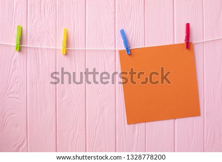 Empty sheet of orange paper on wooden background. An orange post it paper with a white paper clip isolated on wooden background 