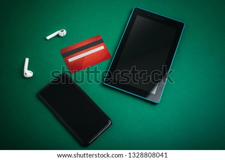Photo of tablet and smartphone, credit card and airpods on green desk