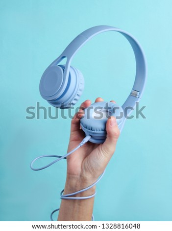 Hand wrapped cable holds headphones on blue background Royalty-Free Stock Photo #1328816048