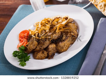 Fried rabbit liver served on white plate with grilled onion and cherry tomatoes