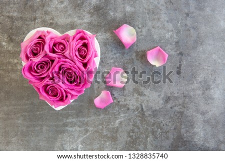 Heart of roses in pink on grey background, from above, free text space