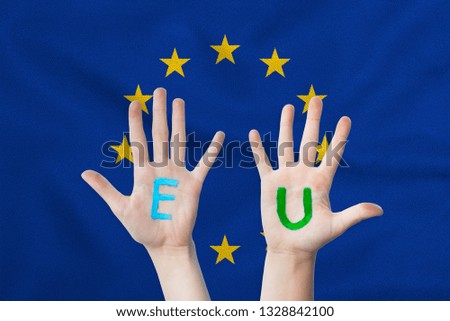 EU inscription on the children's hands against the background of a waving flag of the European Union.