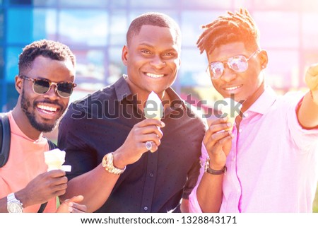 a group of three friends African American guy eating ice cream in a waffle horn and photographing selfie on phone in the summer in the park