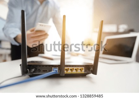 Wireless router with three antennas and cable connected. Man using smartphone in background