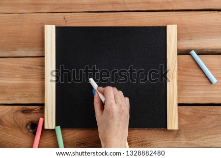 Female hand writing chalk on black Board in wooden frame on wooden background
