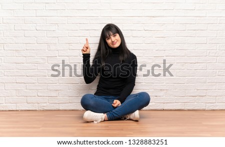 Woman sitting on the floor showing and lifting a finger in sign of the best