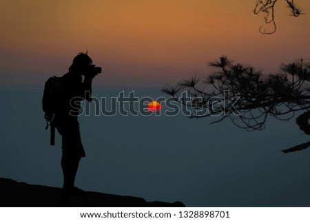 Vintage style of abstract blurred as orange light autumn. The young photographer on mountains and trees, looking at the scenery during golden sunrise background. Travel concepts and summer holidays.