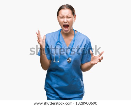 Young caucasian doctor woman wearing medical uniform over isolated background crazy and mad shouting and yelling with aggressive expression and arms raised. Frustration concept.