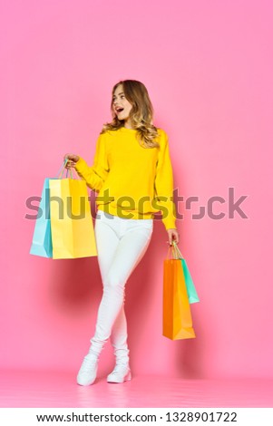 Beautiful woman in a yellow sweater sneakers and pants holding bags in the hands of shopping                  