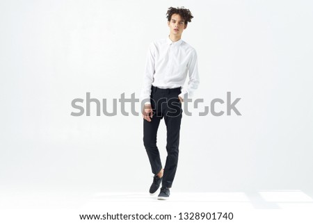 young man with curly hair in trousers shirt and classic shoes is standing in a bright room                 