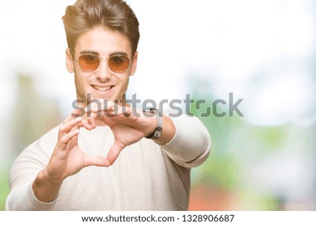 Young handsome man wearing sunglasses over isolated background smiling in love showing heart symbol and shape with hands. Romantic concept.