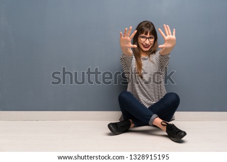 Woman with glasses sitting on the floor counting ten with fingers