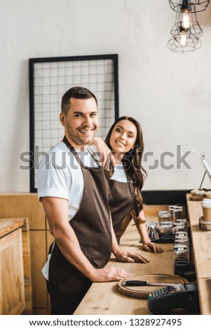cashiers standing and smiling behind wooden bar counte in coffee house