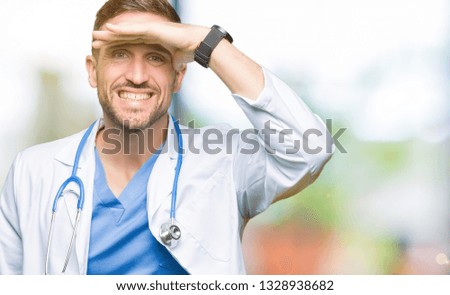 Handsome doctor man wearing medical uniform over isolated background very happy and smiling looking far away with hand over head. Searching concept.