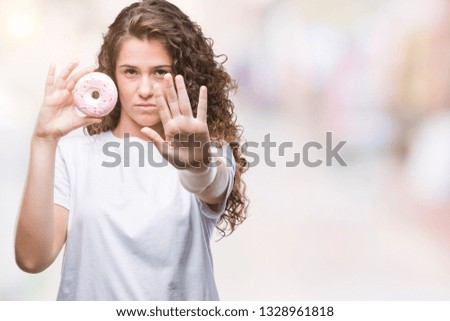 Young brunette girl eating donut over isolated background with open hand doing stop sign with serious and confident expression, defense gesture