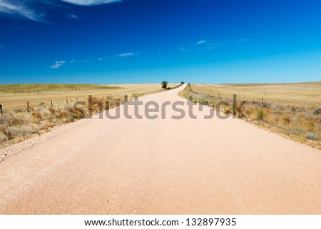 Dirt road in country Australia stretches into the distance under a blue sky