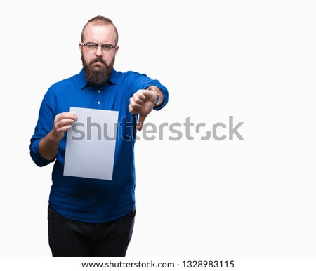Young hipster man wearing glasses and holding blank paper over isolated background with angry face, negative sign showing dislike with thumbs down, rejection concept