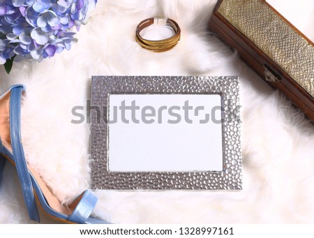 Beautiful silver frame with feminine accessories on white fur. Fashion background.