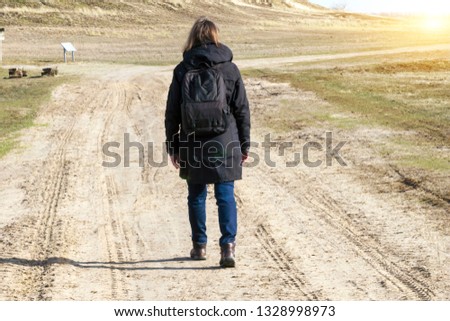 Stock Photo of Caucasian woman in black coat arms raised on empty road towards sunset horizontal
