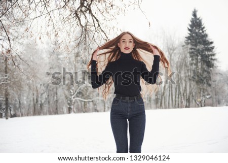 In the clearing. Pretty girl with long hair and in black blouse is in the winter forest.