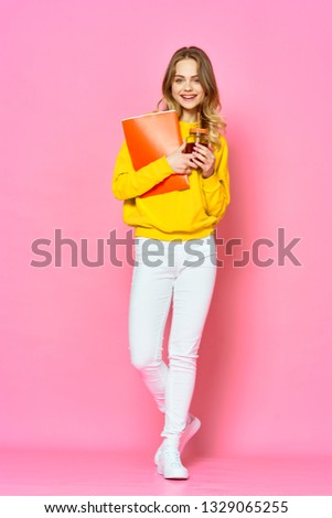 Cheerful pretty woman in a yellow sweater with a drink in her hands and a folder for papers pink background
