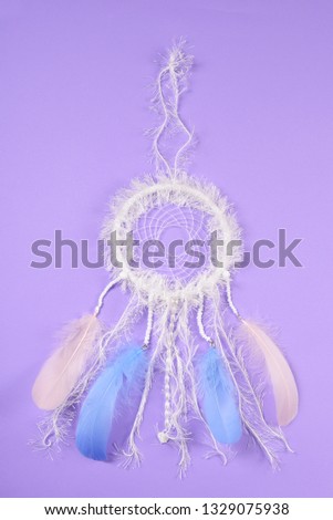 beautiful white dreamcatcher with blue and pink feathers on lilac paper background.