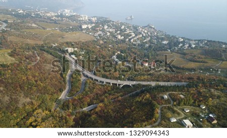 Aerial landscape view of a beautiful bay with forest and hills, small town, and motorway. Shot. Beautiful foggy scenery of autumn yellow fields, highway, and coastal city near the sea.