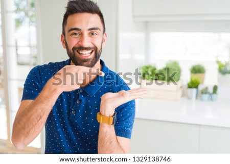 Handsome hispanic man at home amazed and smiling to the camera while presenting with hand and pointing with finger.