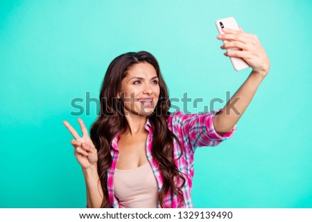 Close up photo beautiful she her lady hold hand arm smart phone new model make take selfies show v-sign say hi wearing casual plaid checkered pink shirt outfit isolated teal bright background