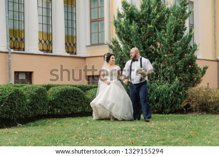 Newlyweds on their wedding day are walking in the park, looking at each other, smiling.