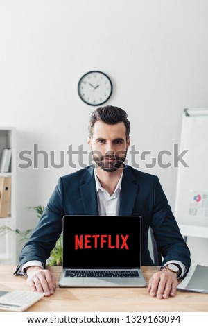 handsome advisor in suit showing laptop with netflix website on screen Royalty-Free Stock Photo #1329163094
