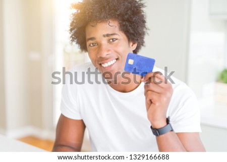 African American man holding credit card with a happy face standing and smiling with a confident smile showing teeth