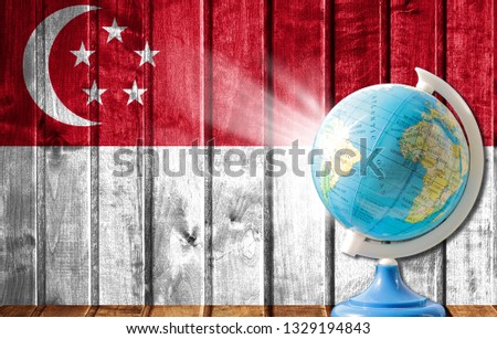 Globe with a world map on a wooden background with the image of the flag of Singapore. The concept of travel and leisure abroad.
