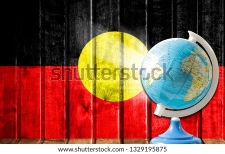 Globe with a world map on a wooden background with the image of the flag of Australian Aboriginal. The concept of travel and leisure abroad.