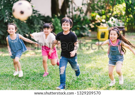Asian and mixed race happy young kids running playing football together in garden. Multi-ethnic children group, outdoor sport exercising, leisure game activity, or childhood fun lifestyle concept Royalty-Free Stock Photo #1329209570